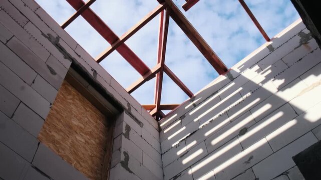 Low angle view of wooden roof frame over unfinished house walls with sunlight casting shadows, showcasing residential construction progress, timber structure and modern building development
