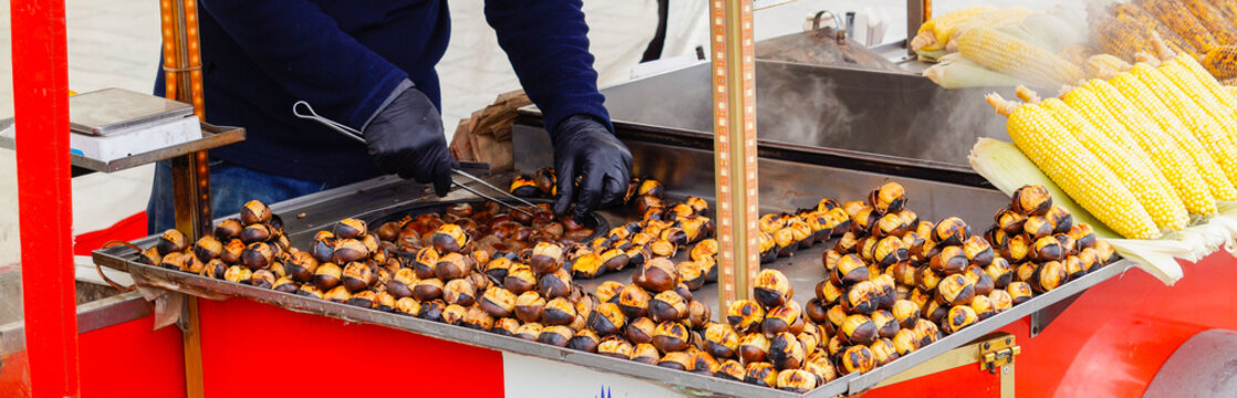 A street food vendor wearing black gloves prepares roasted chestnuts and boiled corn at a bright red stall typical of Turkish street culture, Turkey, Istanbul