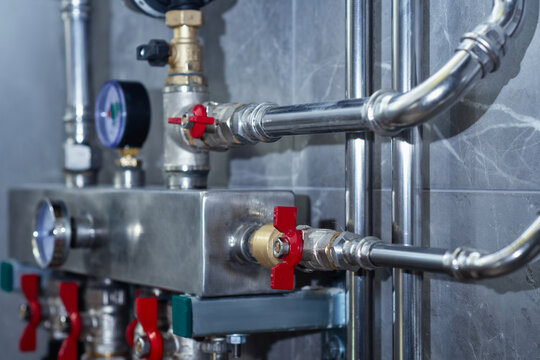 Water distribution manifold with red ball valves and manometers in a boiler room. Plumbing installation for residential heating or water supply system with industrial aesthetic.