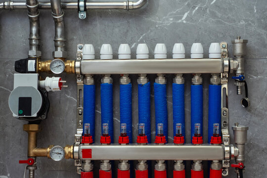 Hydronic heating collector with red and blue insulated pipes and thermal actuators. Modern home climate control technology and energy efficient water distribution system.