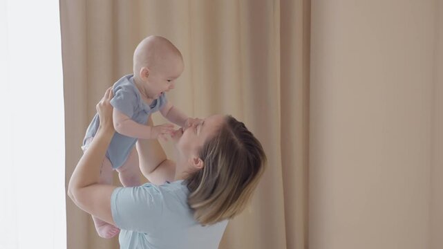 Caucasian mother lifts baby for airplane play, joyful movement and giggles, secure handhold, open window light, airy motion, playful bond, energetic fun