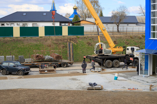 Mobile crane next to a blue building under construction at a construction site during work. Frame of the building under construction in the spring.