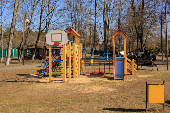 Wooden children's playground equipment with an orange slide and blue climbing elements. The colorful playground is in a city park