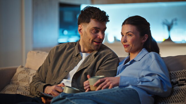 Laughing pair watching television discussing tv show domestic couch closeup
