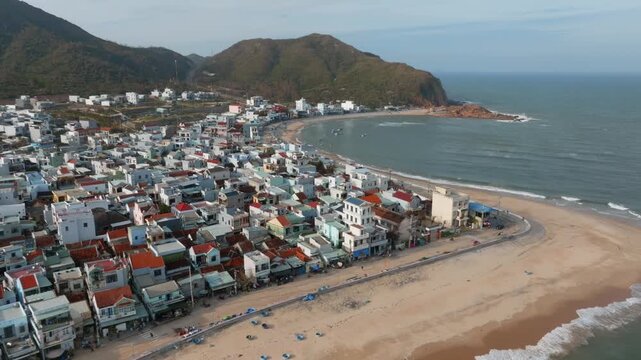Aerial view of the coastal town of Nhon Hai, Quy Nhon, Binh Dinh, Vietnam, with its colorful houses lining the sandy beach and the turquoise sea stretching to the horizon.