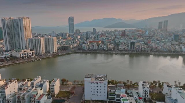 Aerial view of  Quy Nhon, Binh Dinh, Vietnam, with its modern skyline, a tranquil Ho Sinh Thai lake, and mountains in the background at sunset.