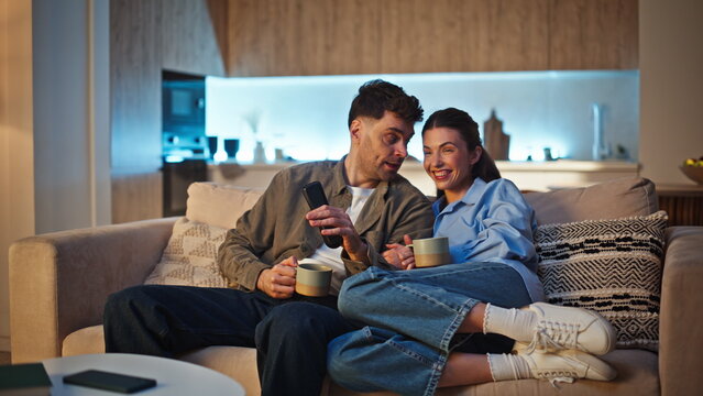 Laughing couple discussing film TV at cozy apartment sofa. Two viewers bonding