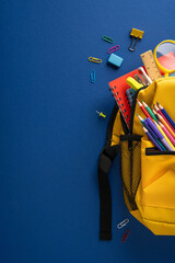 Yellow vertical backpack with colorful pencils, red notebook and school supplies on blue background for back to school © ActionGP
