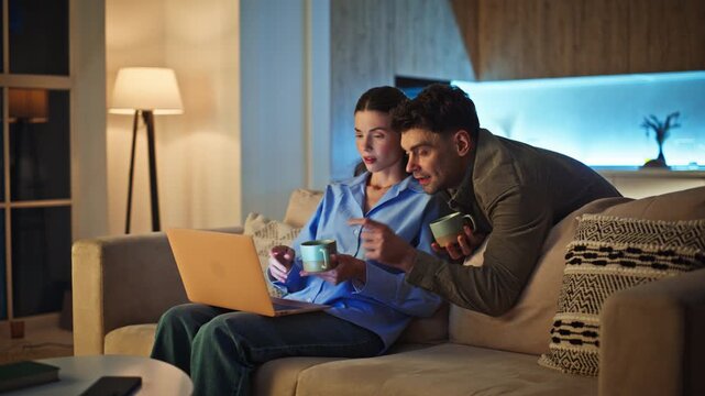 Evening couple looking computer at living room. Domestic man woman cuddling sofa