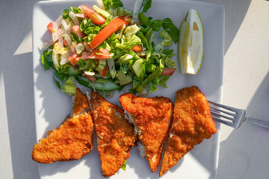 Top view of crispy fried haddock fish with fresh garden salad and lemon