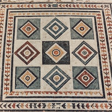 Ancient mosaic floor with geometric diamond patterns. Intricate tesserae create colorful tiles, showing detailed artistry from old civilization ruins. This is historical site.