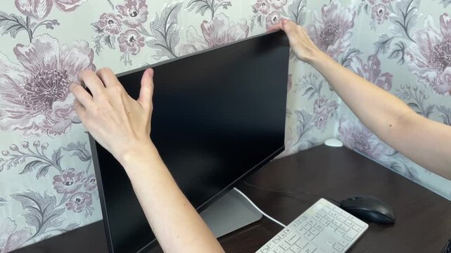 She carefully arranges computer display. Woman correctly aligns her monitor for clear viewing. Woman meticulously places her computer screen in perfect position for comfortable use