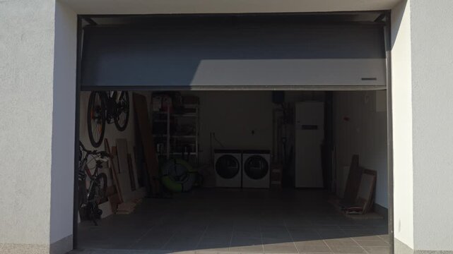 Sectional garage door is closing while a hand holds remote control outside. Concept of residential garage access and automatic operation