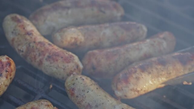Metal tongs turn sausages on a barbecue grill in close up. Food preparation and outdoor cooking concept