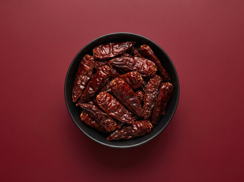 Top view of fresh chipotle chili dried whole in a bowl on a red background
