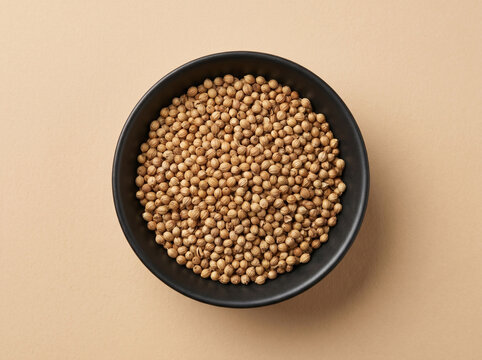 Top view of fresh coriander seeds whole seeds in a bowl on a beige background