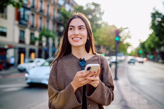 Young woman confidently navigating urban environment, connecting with technology, and enjoying city life during a sunny day