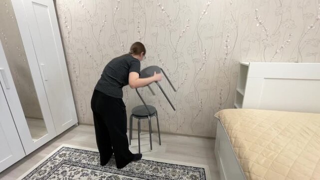 Woman arranging stackable stools beside bed, interior stylist aligns three metal stools in corner, testing balance, optimizing small space, patterned rug and neutral bedspread visible