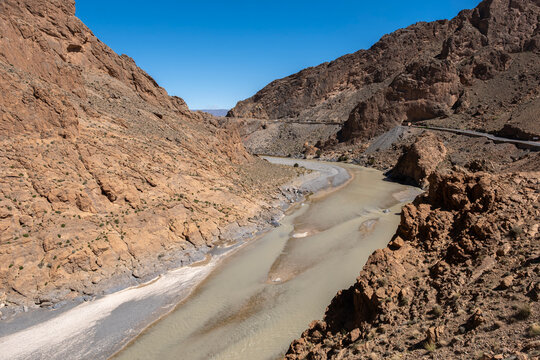 wide angle view of the Ziz River winding through a deep rocky gorge with dramatic cliffs in the High Atlas Mountains of Morocco under a clear blue sky
