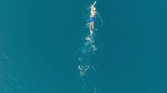 Athlete boy trains sport swimming freestyle in open sea overhead shot