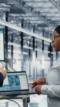 Vertical video Female manager and coworker review microchip factory diagnostic readouts to prevent downtime. Management executives study semiconductor manufacturing plant data, doing quality control