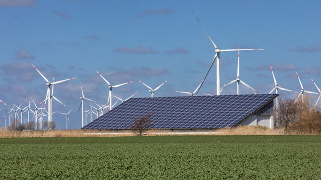 Landwirtschaftliches Geb&auml;ude mit Solardach, Photovoltaik, Solarzellen bei Reu&szlig;enk&ouml;ge an der Nordsee in Nordfriesland, Schleswig-Holstein, dahinter Windr&auml;der