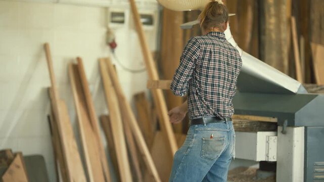 Carpenter using a thickness planer machine in his workshop