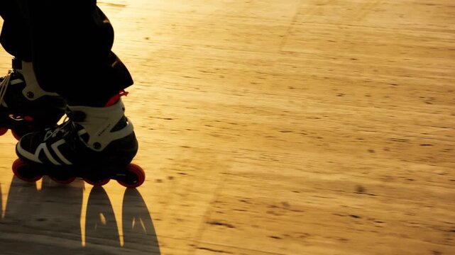 Low angle extreme close-up of orange-wheeled inline skates casting dramatic shadows on warm golden wooden promenade at sunset. Active sport, speed and summer freedom concept.
