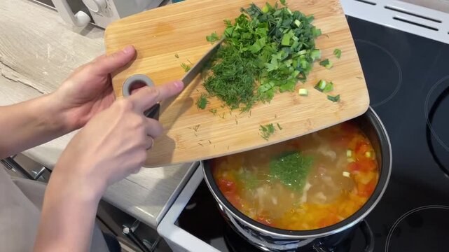 sprinkling chopped parsley into hot soup pot, hands tipping cutting board and scraping bright green herbs into simmering broth to finish dish, fresh aroma and vibrant color uplift presentation