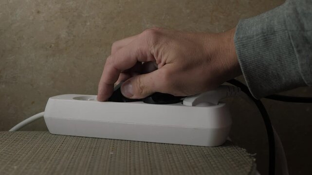 Adult safely unplugs device from strip. Closeup of hand removing plug from electrical strip indoors. Indoor scene highlighting careful disconnection of electrical device from power strip for safety