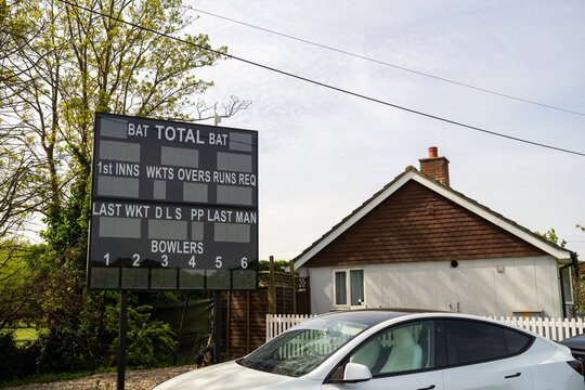 cricket scoreboard in residential area with white car and house under cloudy sky