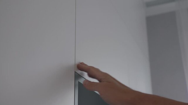 Hand opening overhead cabinet closeup showing white minimalist interior hinge detail, homeowner reaching for item on top shelf, gentle natural light, quiet domestic routine