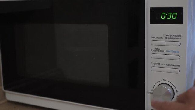 A home cook presses buttons on a microwave oven. Food begins to reheat. Food is reheated in a plastic container. The reheating process begins