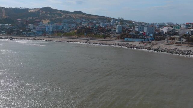 A coastal town iof Nhon Ly, Quy Nhon, Binh Dinh, Vietnam with colorful buildings nestled against a hillside overlooking the sea. The ocean waves gently lap the shore, creating a serene atmosphere.