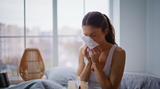 Woman blowing runny nose holding napkin sitting comfortable home bed closeup