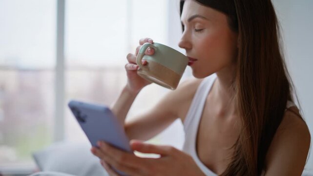 Morning girl hands scrolling smartphone sipping tea cup enjoy time alone closeup