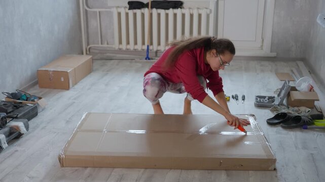 Woman Assembles Furniture. Asian Female Preparing Tools And Parts For Furniture Setup At Home. Young Woman Carefully Unboxes And Arranges Furniture Pieces On Apartment Floor For Assembly
