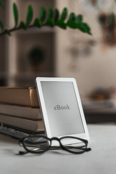 Minimal workspace with ebook tablet, eyeglasses and books on bright desk. Calm productive setup for freelancer, planning tasks, business reading and focused morning routine at home office.