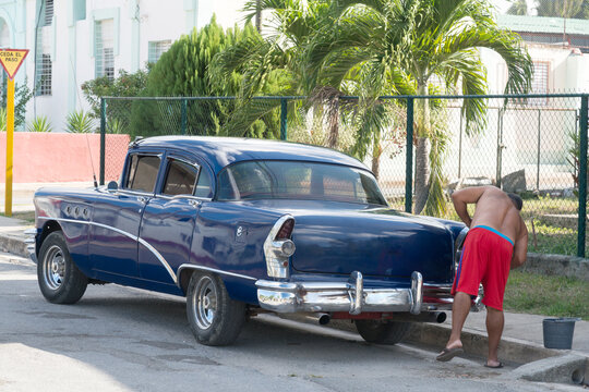 Cuba, Cienfuegos.  Man washing his 1950's era American automobile.