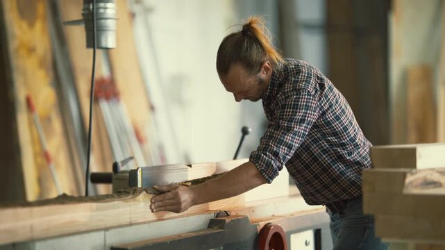 Carpenter planing a wood plank on a jointer machine