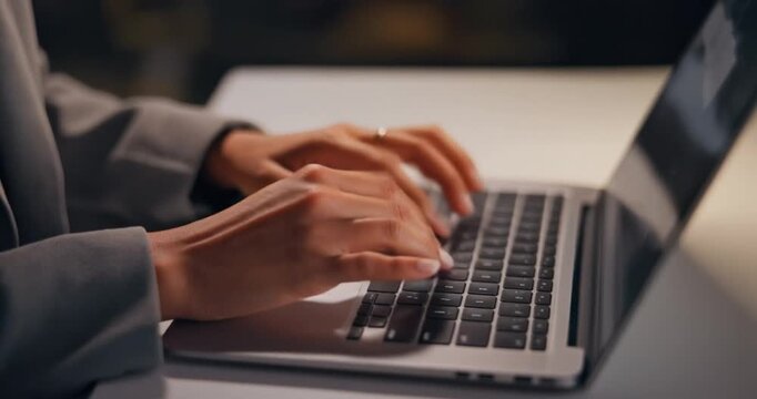Close up of hands typing on a laptop computer keyboard in slow motion.