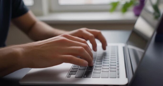 Close up shot of man hands typing on laptop computer keyboard in modern workspace.