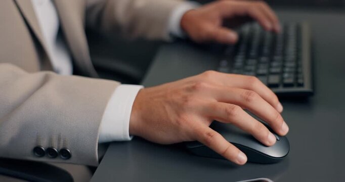 Business person hands using computer mouse and keyboard at desk in office setting.