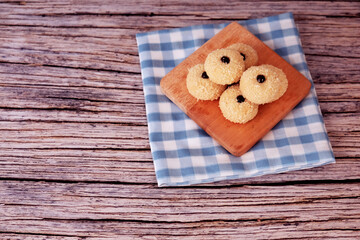 Fototapeta premium Kue Monde Susu or cookies rest on a wooden board. Board sits atop a blue-and-white checkered napkin. Napkin lies on a rustic wooden table. Ideal for cozy cafe or home baking themes