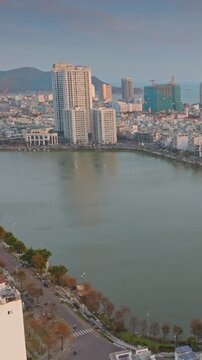 Aerial view of  Quy Nhon, Binh Dinh, Vietnam, with its modern skyline, a tranquil Ho Sinh Thai lake, and mountains in the background at sunset.