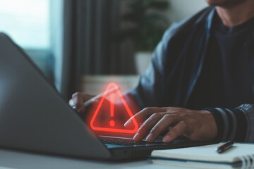 Cyber security warning concept. Businessman typing on laptop, showing alert symbol and data risk notification. Cybersecurity, system error, data protection, hacking prevention, IT security services. © THAWEERAT