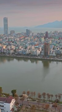 Aerial view of  Quy Nhon, Binh Dinh, Vietnam, with its modern skyline, a tranquil Ho Sinh Thai lake, and mountains in the background at sunset.