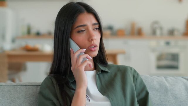 Sad frustrated Indian woman at home talking mobile phone upset stressed problem breakup worry mortgage loan insurance failure loss Arabian girl Latina female use telephone trouble disappointed indoors