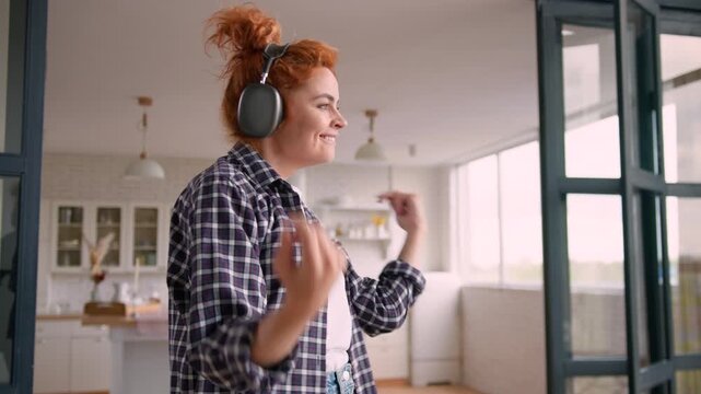 Happy Caucasian woman dancing couch at home listening music in wireless headphones female moving smiling having fun relaxing fooling around enjoying song audio sound freedom excited carefree indoors