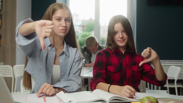 Upset Caucasian teen girls showing thumbs down exam inside class frustration schoolgirls dissatisfied students classmates teenagers learning lesson fail education disappointment bad studying problem